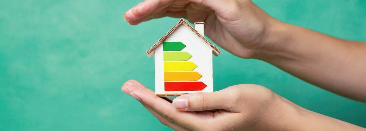 Verduurzamen, Energiebesparing; een huisje met energielabels wordt tussen 2 handen gehouden op een groene achtergrond