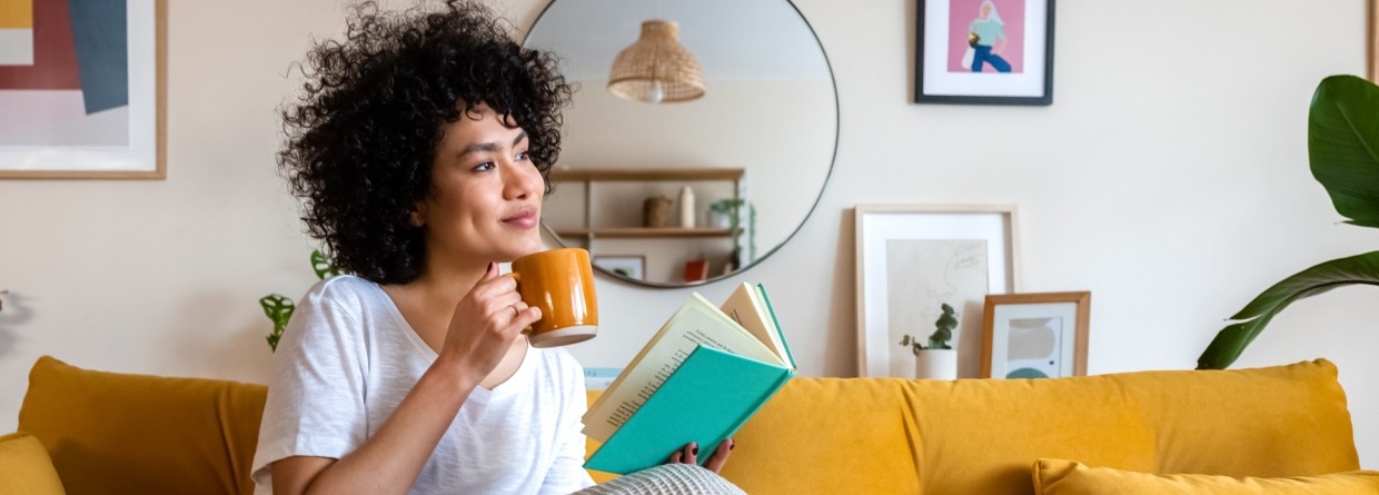 Een ontspannen Afro-Amerikaanse vrouw leest thuis een boek en drinkt koffie op de bank