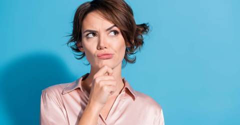 Denkende vrouw met haar hand op haar kin draagt een roze satijnen blouse en stata voor een blauwe achtergrond