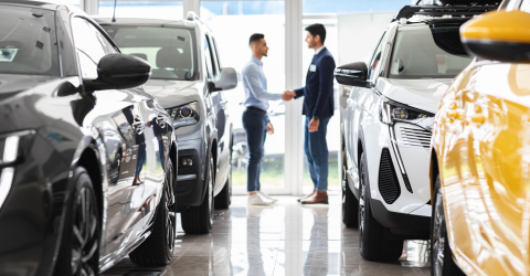 Auto lease; klant en verkoper schudden elkaar de hand in een showroom met auto's